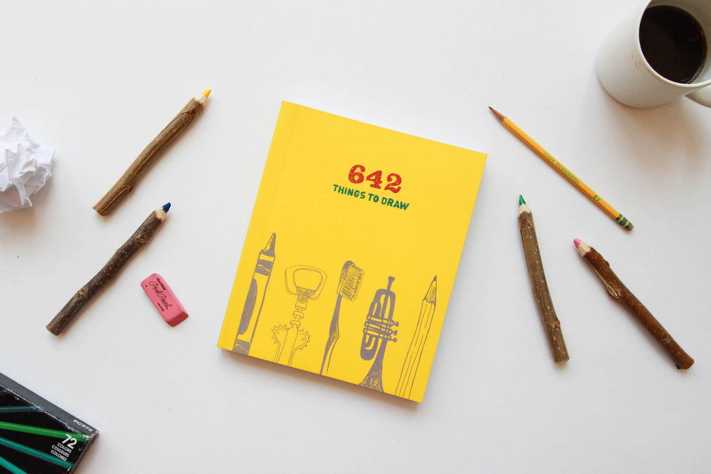 Two small ceramic animals sit beside a set of colorful paint brushes on a wooden surface.